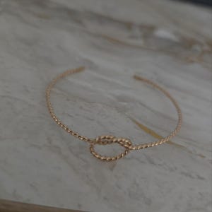 May include: A gold-toned cuff bracelet featuring a twisted rope texture throughout the band. The center of the bracelet displays a decorative knot design, and the piece has an open-ended construction, allowing for easy adjustment on the wrist.