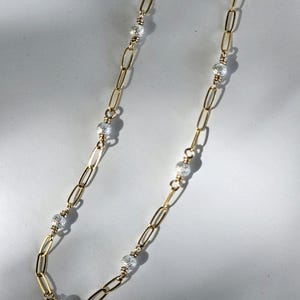 May include: A gold chain necklace with silver beads. The chain is made of small, linked ovals. The beads are round and have a textured surface.