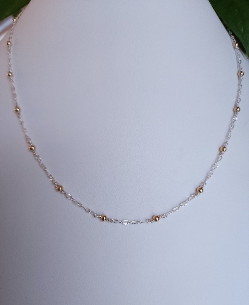 Puede incluir: Un collar de cadena de plata con cuentas doradas. El collar es delicado y simple, lo que lo convierte en una pieza de joyer&iacute;a vers&aacute;til.