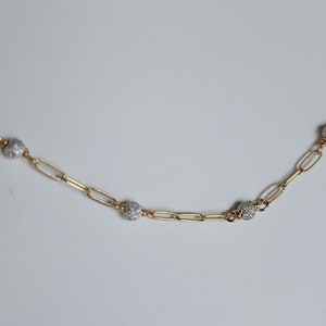 Puede incluir: Un collar de cadena dorada con peque&ntilde;as cuentas redondas texturizadas. Las cuentas son de metal plateado.