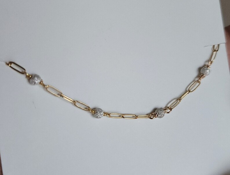 Puede incluir: Un collar de cadena dorada con peque&ntilde;as cuentas redondas texturizadas. Las cuentas son de metal plateado.