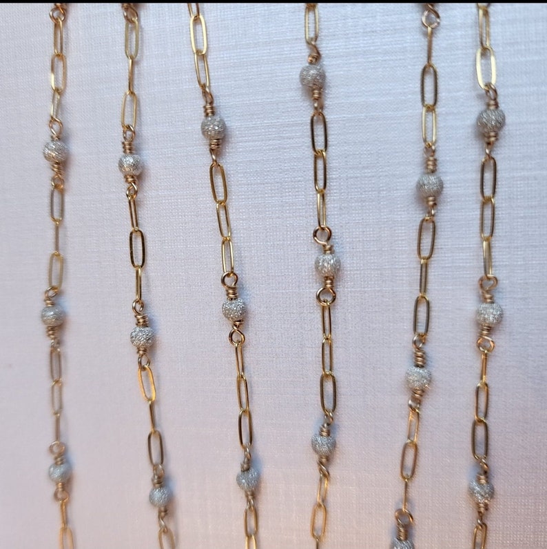 Puede incluir: Cinco cadenas de oro con cuentas de plata. Cada cadena tiene una longitud diferente y las cuentas est&aacute;n espaciadas uniformemente.