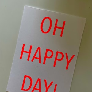 K&ouml;nnte beinhalten: Eine wei&szlig;e Karte mit dem Schriftzug "OH HAPPY DAY!" in leuchtend roten Buchstaben. Die rechteckige Karte hat ein schlichtes Design, ideal f&uuml;r eine Gru&szlig;botschaft oder einen besonderen Anlass.