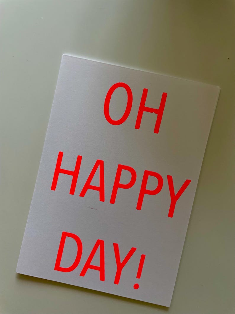 K&ouml;nnte beinhalten: Eine wei&szlig;e Karte mit dem Schriftzug "OH HAPPY DAY!" in leuchtend roten Buchstaben. Die rechteckige Karte hat ein schlichtes Design, ideal f&uuml;r eine Gru&szlig;botschaft oder einen besonderen Anlass.