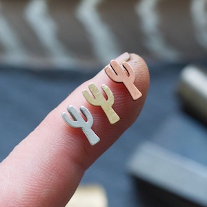May include: Three small cactus-shaped earrings in silver, gold, and rose gold.