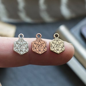 May include: Three silver, rose gold, and gold 20-sided dice charms. The charms are small and are held in a person's hand.