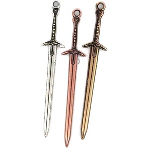 May include: Three miniature sword charms in silver, copper, and gold finishes. Each sword charm has a detailed design and a loop at the top for attaching to jewelry or other crafts.
