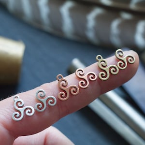 May include: Five metal charms in different finishes, including silver, gold, and rose gold, each featuring a triple spiral design.