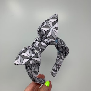 May include: A gray and white headband with a geometric pattern. The headband is tied in a bow at the top.