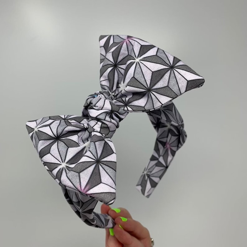 May include: A gray and white headband with a large bow. The bow is made of fabric with a geometric pattern of stars.