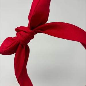 May include: A red fabric headband with a knotted bow. The headband is made of a soft, stretchy fabric and is perfect for adding a touch of style to any outfit.