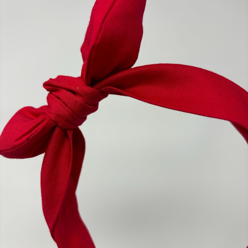 May include: A red fabric headband with a knotted bow. The headband is made of a soft, stretchy fabric and is perfect for adding a touch of style to any outfit.
