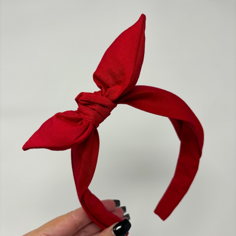 May include: A red fabric headband with a large bow on top. The headband is made of a soft, stretchy fabric and is perfect for adding a touch of style to any outfit.