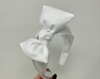 May include: A white fabric headband with a large, knotted bow. The headband is made of a soft, stretchy material and is perfect for adding a touch of elegance to any outfit.