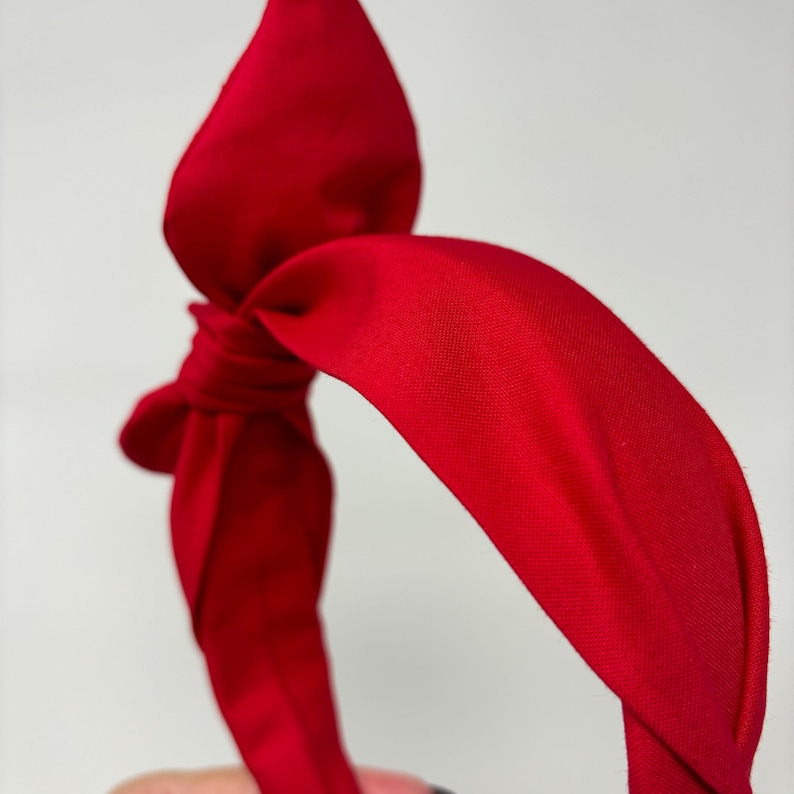 May include: A red fabric headband with a knotted bow on top.