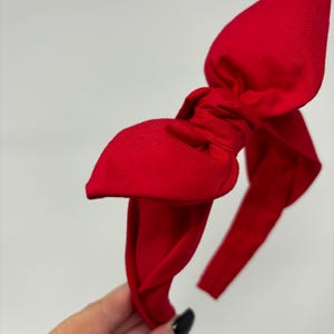 May include: A bright red fabric headband with a large bow. The headband is twisted and tied into a knot at the top of the bow.