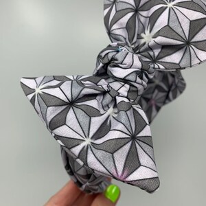 May include: A gray and white patterned headband with a large bow. The pattern is geometric and resembles a starburst.
