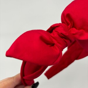 May include: A bright red fabric headband with a large bow. The headband is made of a soft, stretchy material and is perfect for adding a touch of style to any outfit.