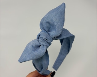 May include: A light blue denim headband with a large bow. The bow is knotted in the center and has two large loops. The headband is a solid color and is made of a soft fabric. This hair accessory is perfect for adding a touch of style.