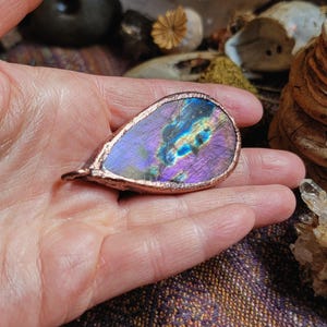 May include: A teardrop-shaped pendant with a copper frame and a iridescent labradorite stone. The stone has a purple, blue, and green color.
