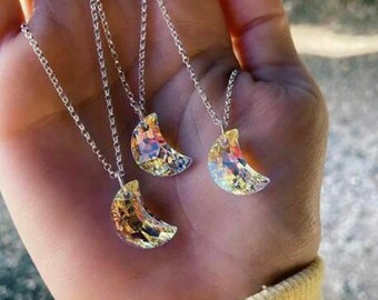 May include: Three silver necklaces with iridescent crescent moon pendants. The necklaces are layered and the pendants are different sizes.