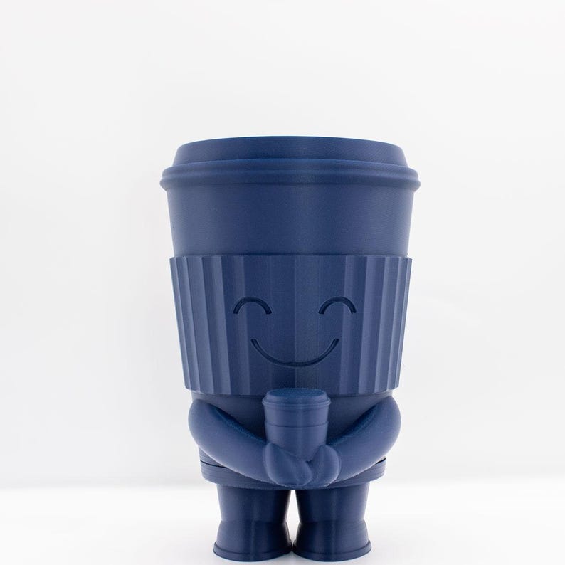 May include: A blue ceramic figurine of a coffee cup with a smiling face holding a smaller coffee cup. The figurine is standing on a white surface.