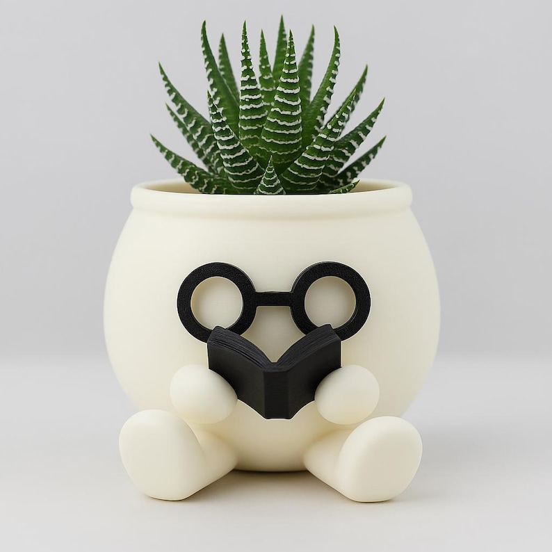 May include: White ceramic planter shaped like a person wearing glasses and reading a book. The planter has a green succulent plant growing inside.