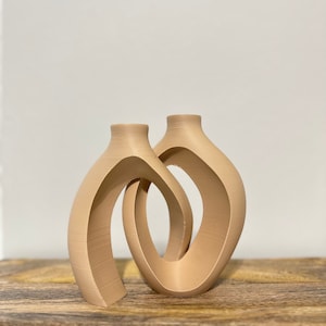 May include: Two beige ceramic vases with a unique, abstract design. The vases are connected and have a curved, open shape.