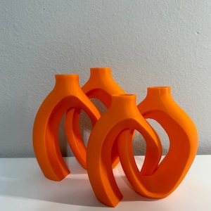 May include: Three orange ceramic vases with a unique, abstract design. The vases are stacked on top of each other, creating a modern and stylish look.