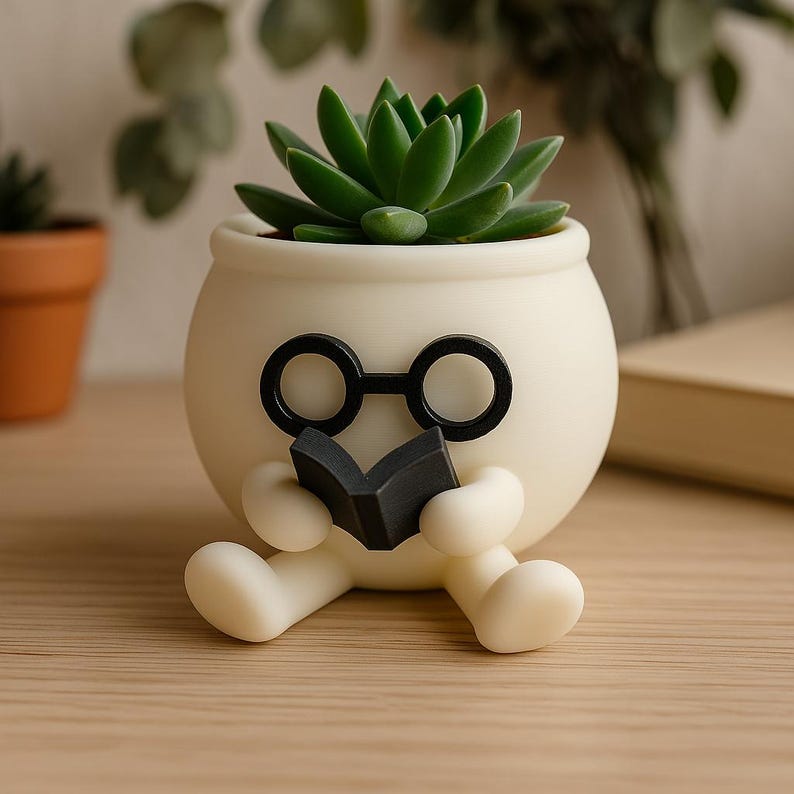 May include: White ceramic planter shaped like a person wearing glasses and holding a book. The planter has a succulent plant growing inside.