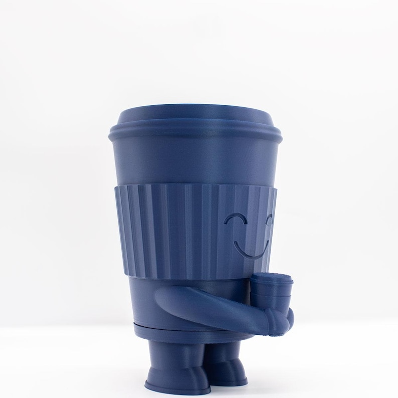 May include: A blue ceramic figurine of a coffee cup with a smiling face. The cup is holding another smaller coffee cup in its hand.