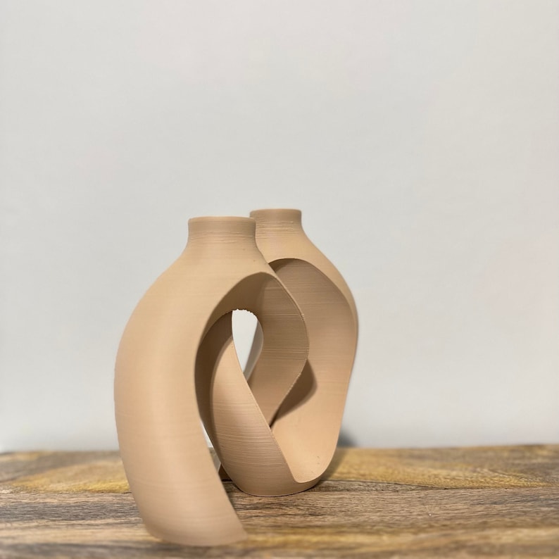 May include: Two beige ceramic vases with a unique, abstract design. The vases are connected and have a curved, organic shape.