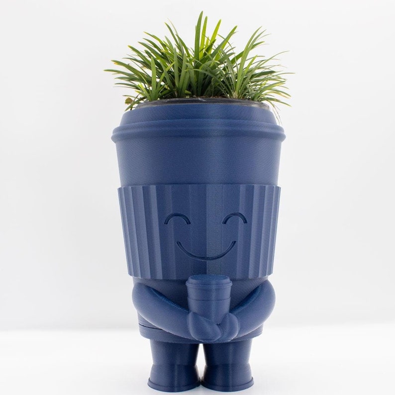 May include: A blue ceramic planter shaped like a smiling coffee cup with a green plant growing inside.