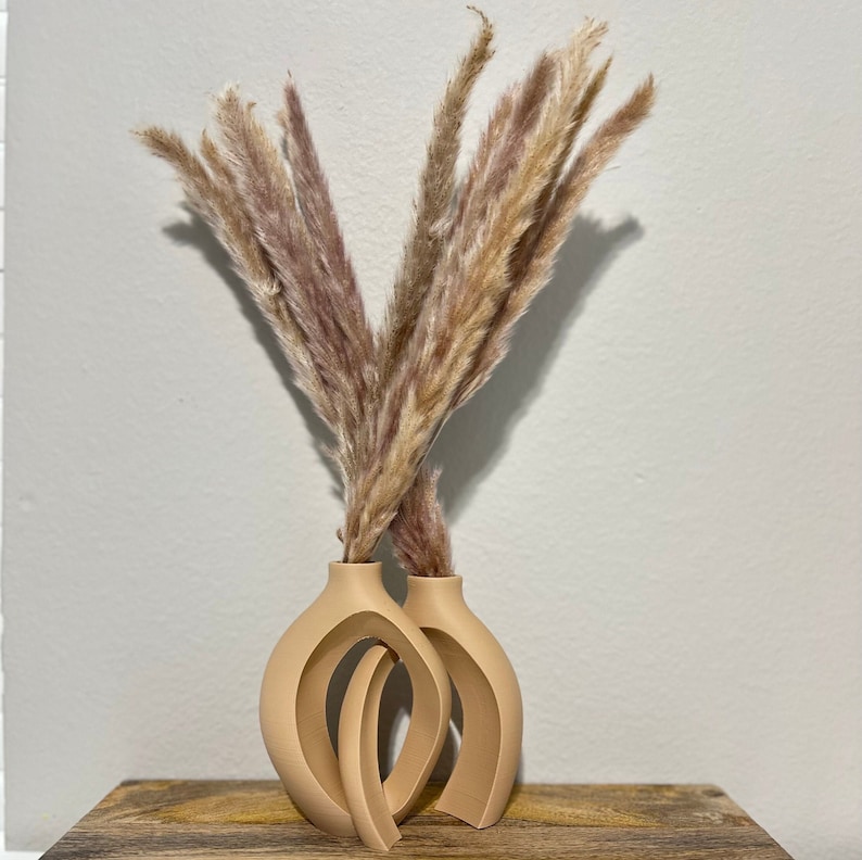 May include: Two beige ceramic vases with an abstract design, holding a bouquet of dried pampas grass.