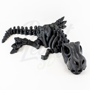 May include: A black 3D printed dinosaur skeleton model. The dinosaur is lying on its side with its head turned to the side. The skeleton is detailed and realistic.