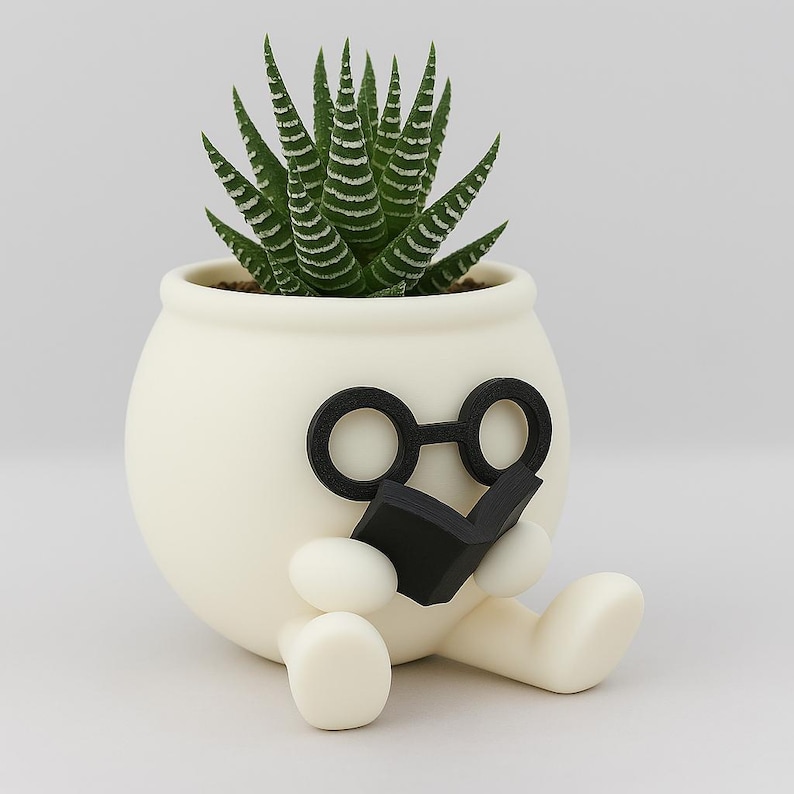 May include: White ceramic planter shaped like a person wearing glasses and reading a book. The planter has a green succulent plant growing inside.