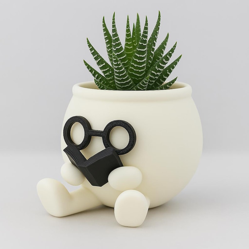 May include: White ceramic planter shaped like a person sitting with legs crossed, wearing round black glasses and holding a black book. The planter has a green succulent plant growing inside.