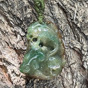 May include: A green jade pendant carved with a dragon and a fish. The pendant is hanging from a green cord with a yellow bead.
