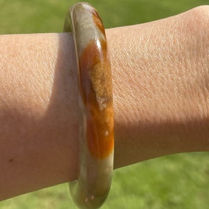 May include: A brown, white, and green jade bangle bracelet. The bangle is smooth and polished.