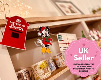 Puede incluir: Decoración navideña con un buzón rojo con la inscripción "Letters to Santa" y un recorte de Minnie Mouse con gorro y bufanda de Papá Noel. Varias tazas son visibles en una estantería debajo.