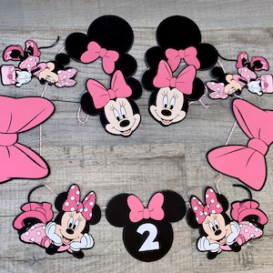 K&ouml;nnte beinhalten: Eine Sammlung von Minnie Mouse-Partydekorationen. Enth&auml;lt schwarze und rosa Minnie Mouse-Kopf-Ausschnitte mit rosa Schleifen, Minnie Mouse-Figuren in rosa gepunkteten Kleidern und eine Zahl 2. Perfekt f&uuml;r eine Geburtstagsfeier.