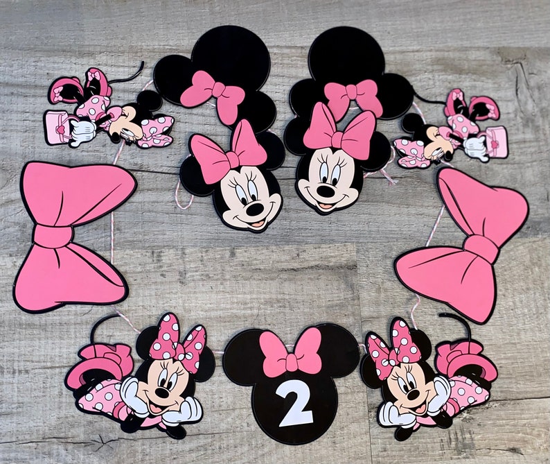 K&ouml;nnte beinhalten: Eine Sammlung von Minnie Mouse-Partydekorationen. Enth&auml;lt schwarze und rosa Minnie Mouse-Kopf-Ausschnitte mit rosa Schleifen, Minnie Mouse-Figuren in rosa gepunkteten Kleidern und eine Zahl 2. Perfekt f&uuml;r eine Geburtstagsfeier.