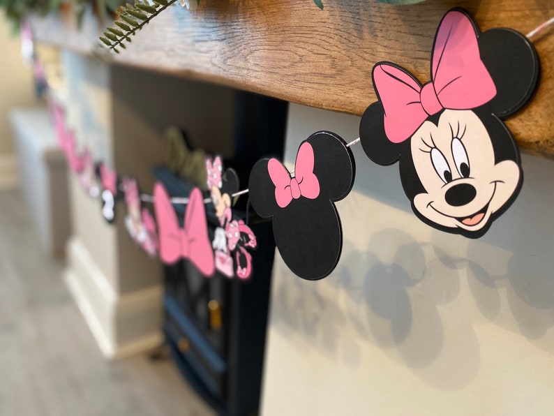 K&ouml;nnte beinhalten: Eine dekorative Girlande mit Minnie Mouse. Die Girlande enth&auml;lt Ausschnitte von Minnie Mouses Kopf, Schleifen und andere Charakterelemente. Das Farbschema ist Schwarz, Rosa und Wei&szlig;, zusammengef&uuml;gt mit wei&szlig;er Schnur. Ideal f&uuml;r eine Party oder Feier.