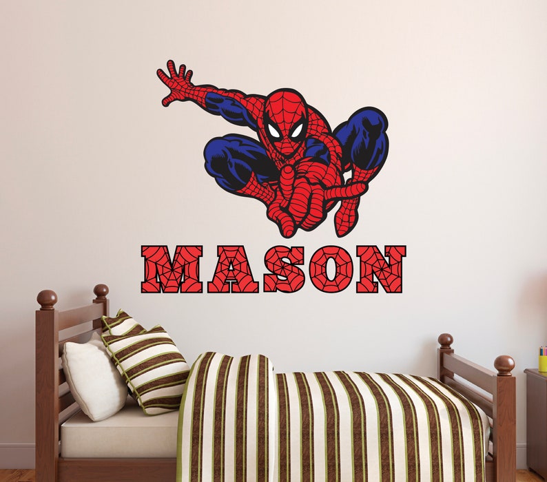 Puede incluir: Un adhesivo de pared Spiderman rojo y azul con un dise&ntilde;o de telara&ntilde;a. El adhesivo est&aacute; sobre una cama de madera marr&oacute;n con una manta a rayas. El nombre "MASON" est&aacute; escrito en letras rojas con un dise&ntilde;o de telara&ntilde;a.