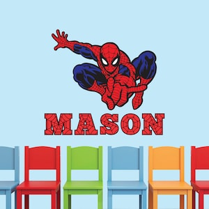 Puede incluir: Un adhesivo de pared de Spiderman rojo y azul con el nombre "MASON" en letras rojas con un patr&oacute;n de telara&ntilde;a. La calcoman&iacute;a est&aacute; en una pared azul claro con cinco sillas de colores en frente.