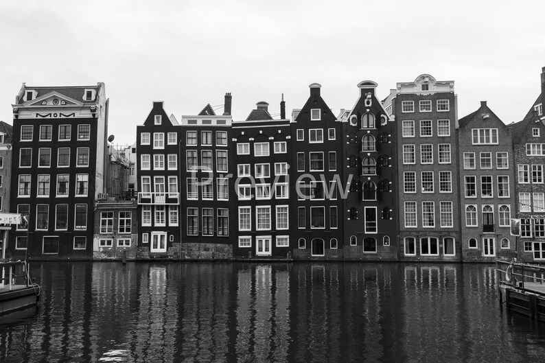 May include: Black and white photo of a row of traditional Dutch canal houses with a reflection in the water.