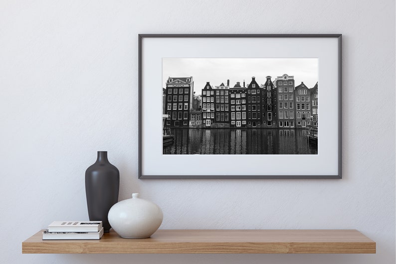 May include: Black and white photograph of a row of traditional Dutch canal houses reflected in the water.