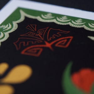 May include: Close-up of a print with a black background and a red, stylized design. The print has a green border with a cream-colored decorative pattern. Yellow and red shapes are visible in the lower portion of the image.
