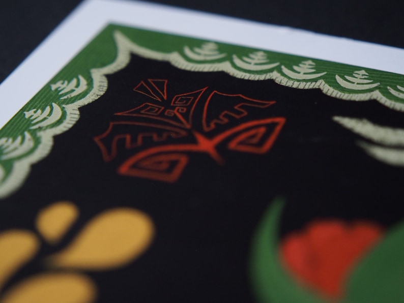 May include: Close-up of a print with a black background and a red, stylized design. The print has a green border with a cream-colored decorative pattern. Yellow and red shapes are visible in the lower portion of the image.