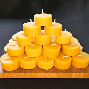 Könnte beinhalten: Eine Pyramide aus 20 gelben Bienenwachs-Teelichtern auf einem Holzbrett.
